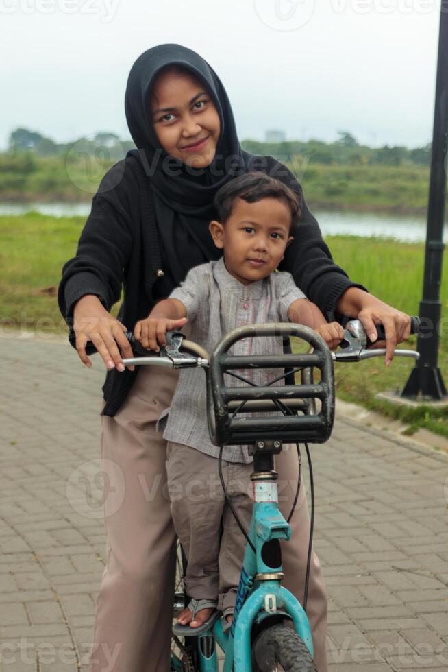 Happy Muslim Sister and Little Brother Riding Bicycle Outdoors photo