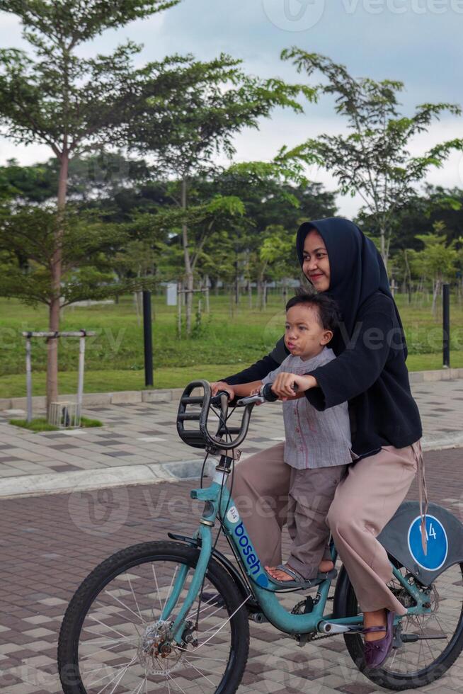 Muslim Sister Riding a Bicycle with Younger Brother in Park photo