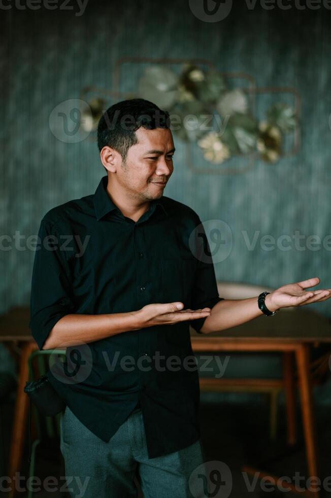 Confident asian man presenting product with smile in modern interior setting photo