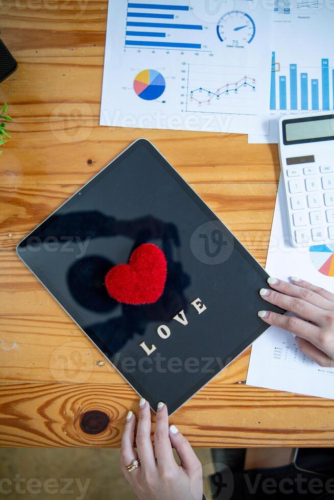 Red heart symbol placed on screen glass of tablet placed on the desk and the heart symbolizes love and friendship for friends and lovers. Red heart symbol concept represents friendship and love. photo