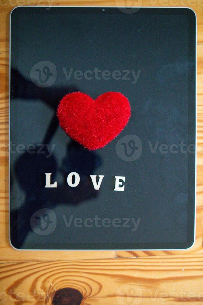 Red heart symbol placed on screen glass of tablet placed on desk and heart symbolizes love and friendship for friends and lovers. Red heart symbol concept represents friendship and love. photo