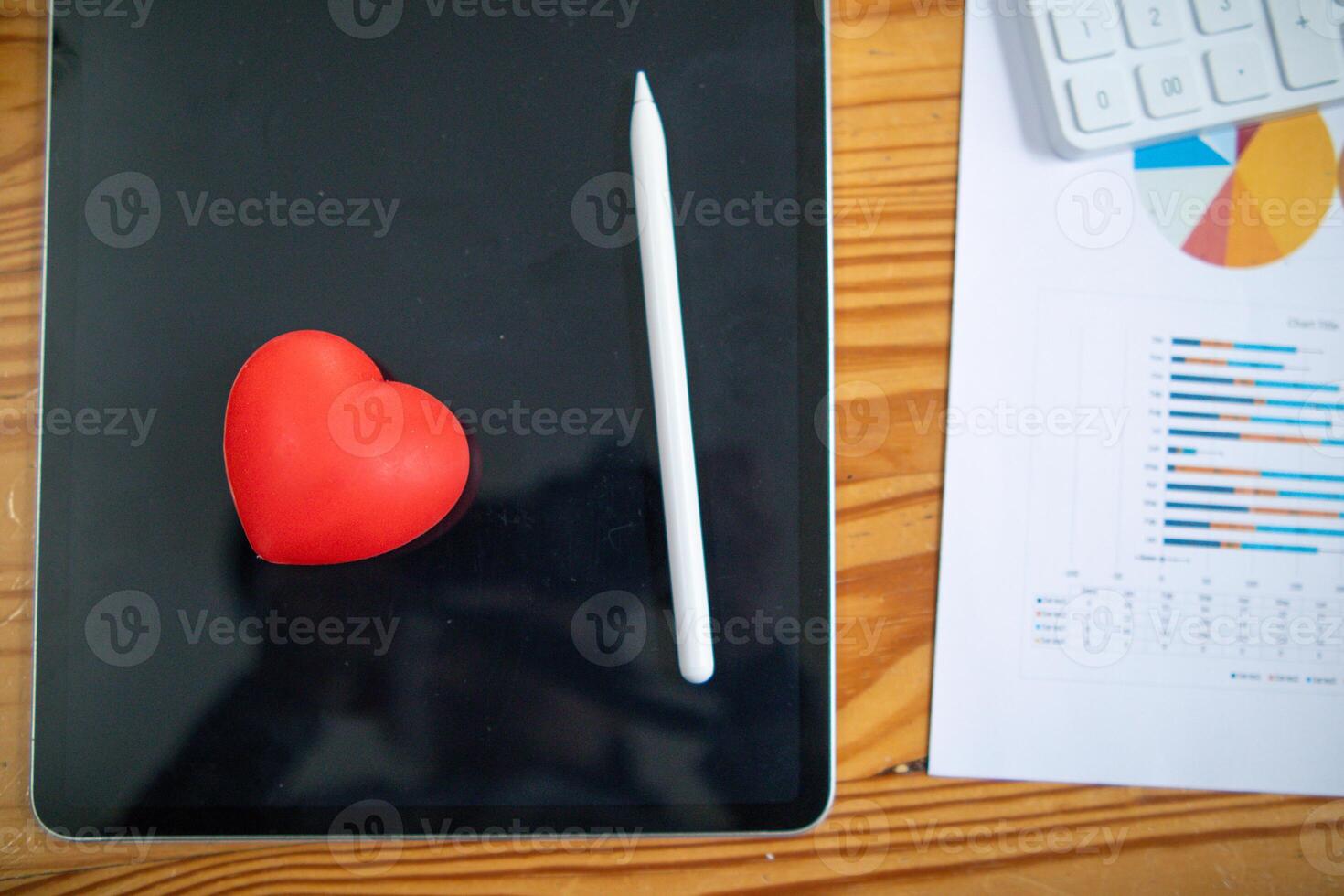 Red heart symbol placed on screen glass of tablet placed on the desk and heart symbolizes love and friendship for friends and lovers. Red heart symbol concept represents friendship and love. photo