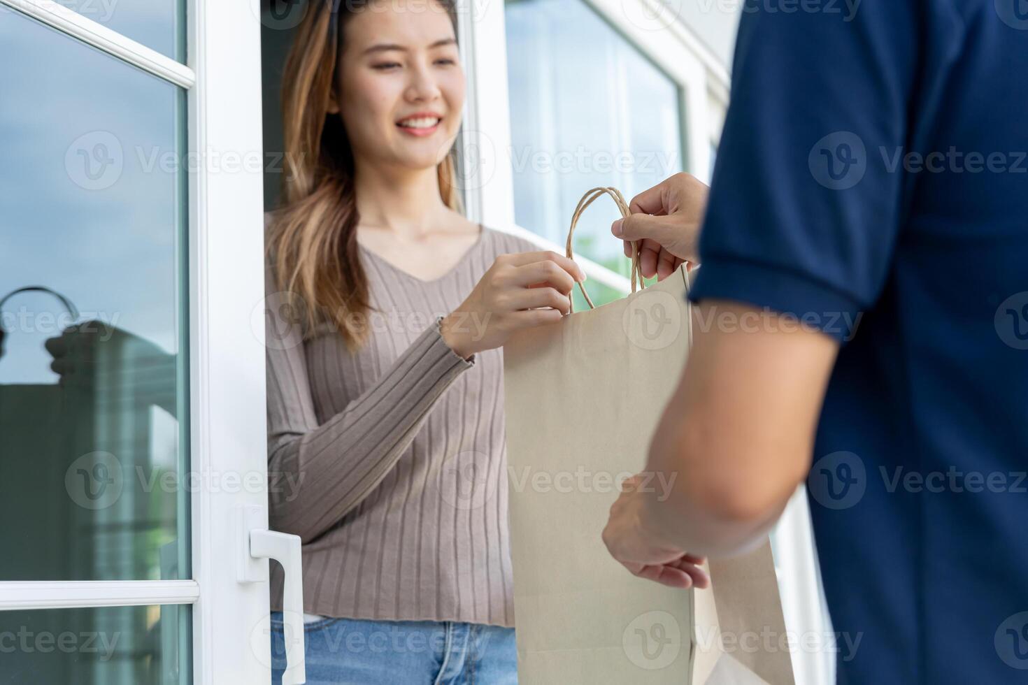 Happy smiling Asian woman receives paper bag parcel of food from courier front house. Delivery man send deliver express. online shopping, paper container, takeaway, postman, delivery service, photo