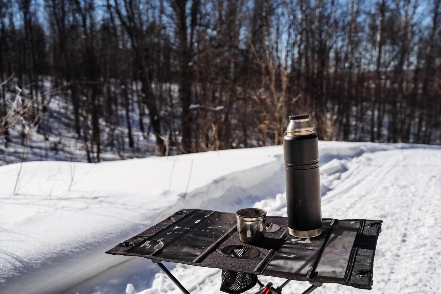 A coffee pot and a thermos on a table in the snow photo