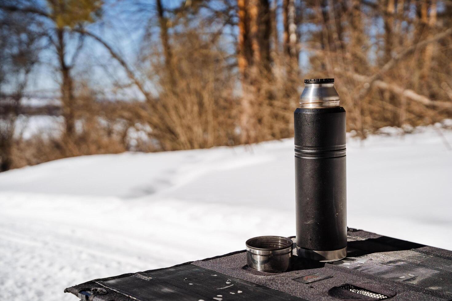 A black and silver thermos sitting on top of a snow covered table photo