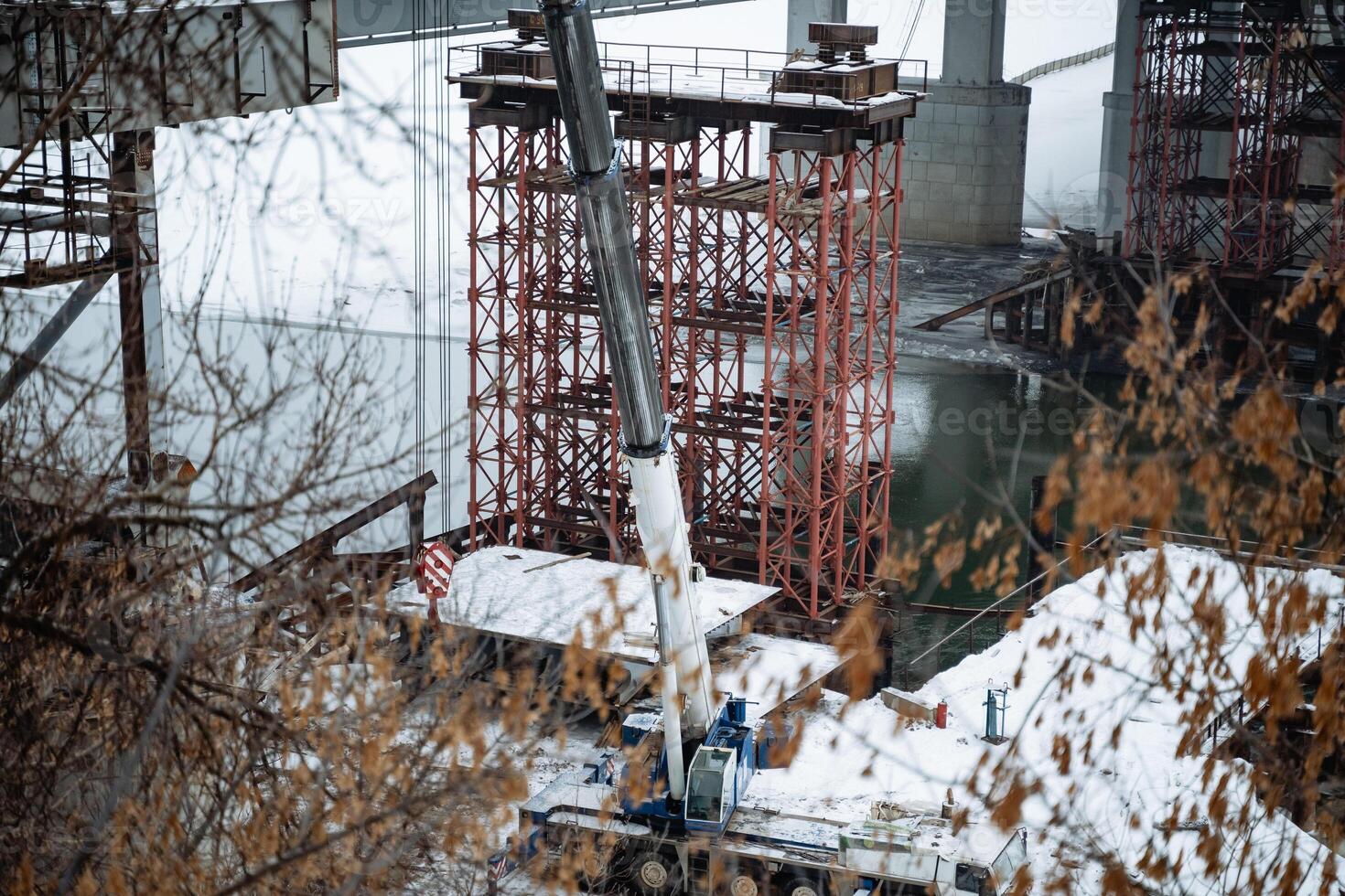A large crane is currently being used for the construction of a bridge that spans over a river, showcasing engineering excellence and skillful planning in infrastructure development photo