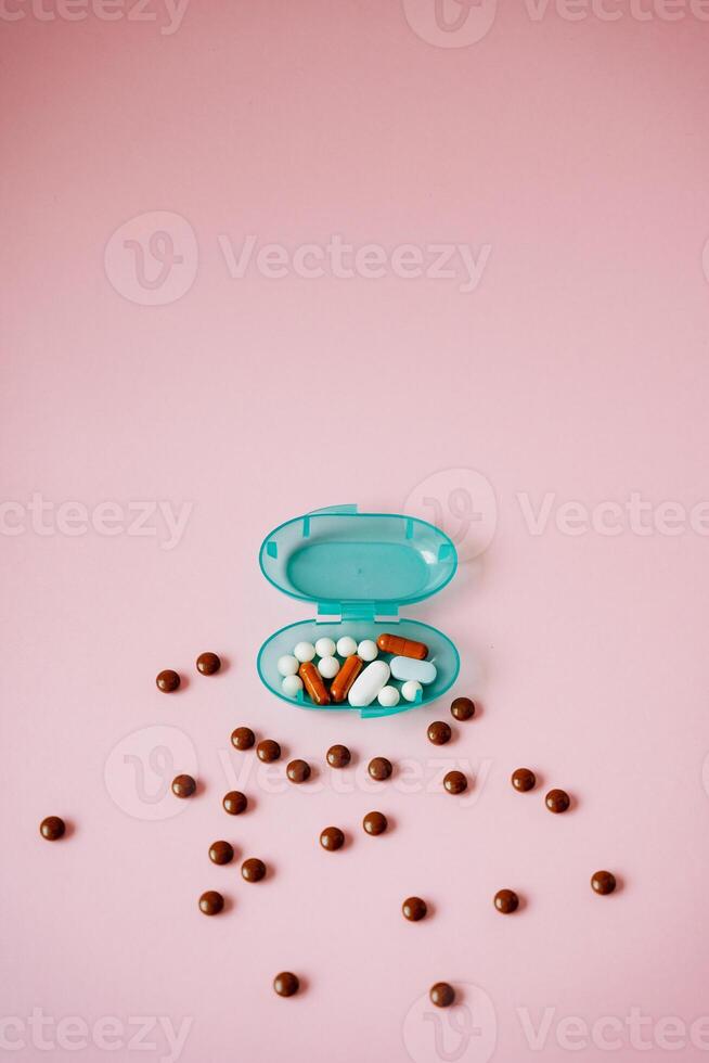 A blue container overflows with colorful pills and chocolate balls, creating a striking contrast against a soft pink background, enhancing its visual appeal and attracting attention photo