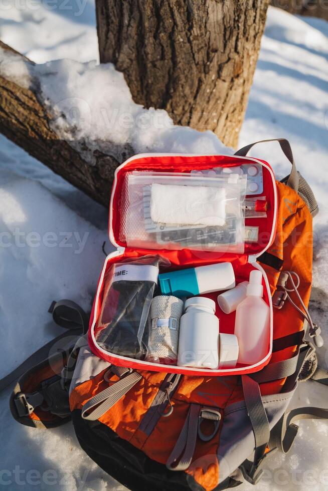 A large backpack that is fully packed with a wide array of essential first aid supplies remains unused and untouched, lying silently in the cold snow, waiting for someone to find it photo