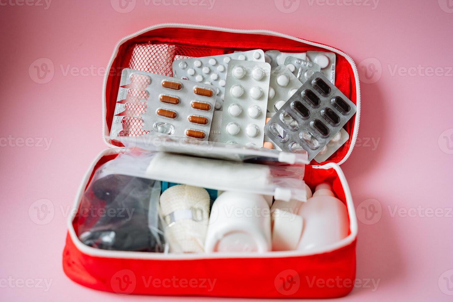 A bright red first aid kit, carefully filled with essential items like various pills, several bandages, and a syringe for medical emergencies, is ready for personal care and health needs photo