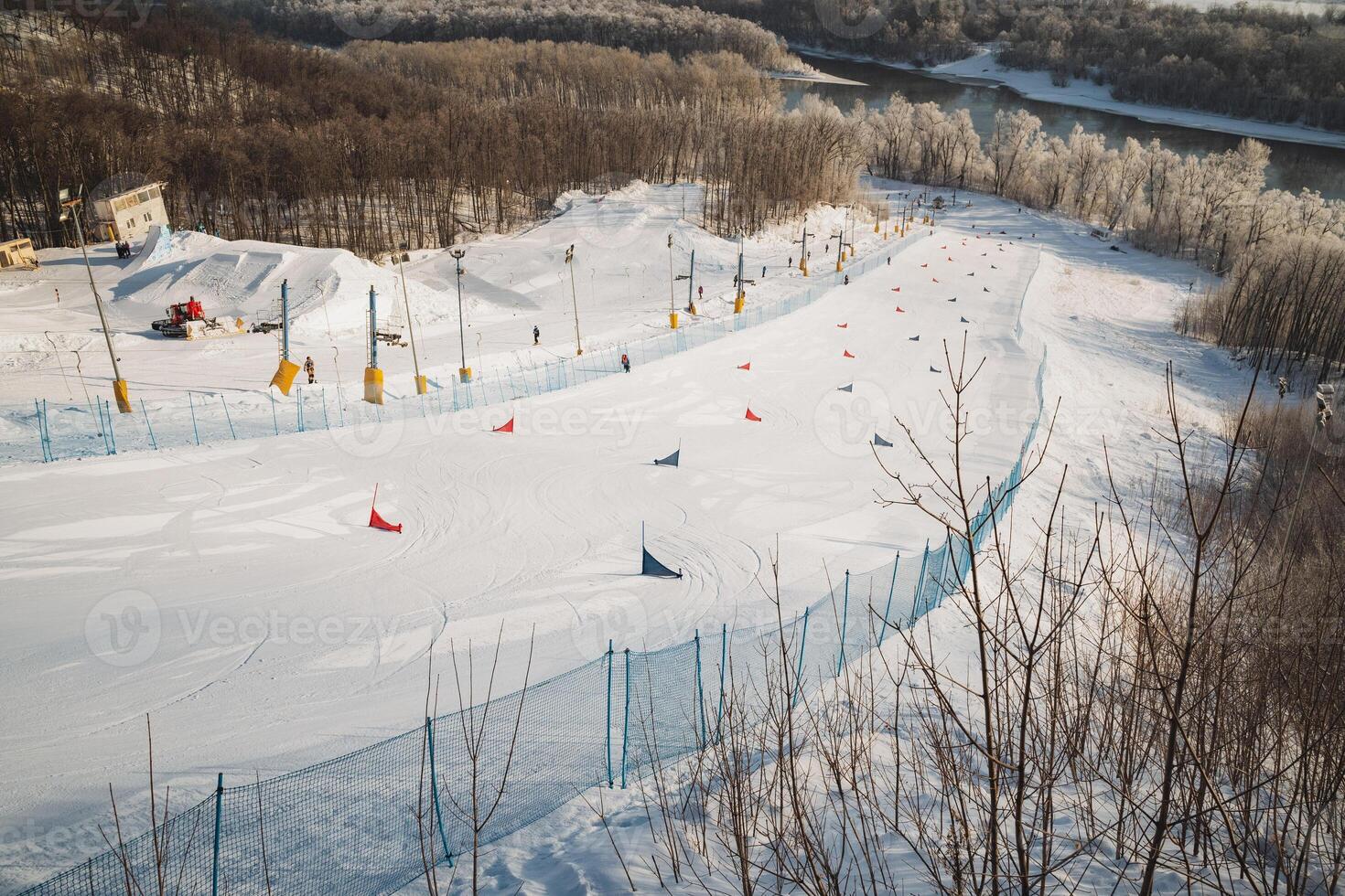 A picturesque snowy ski slope is adorned with a bright blue fence, and majestic trees can be seen in the beautiful background, creating a perfect winter scene for skiers and snowboarders photo