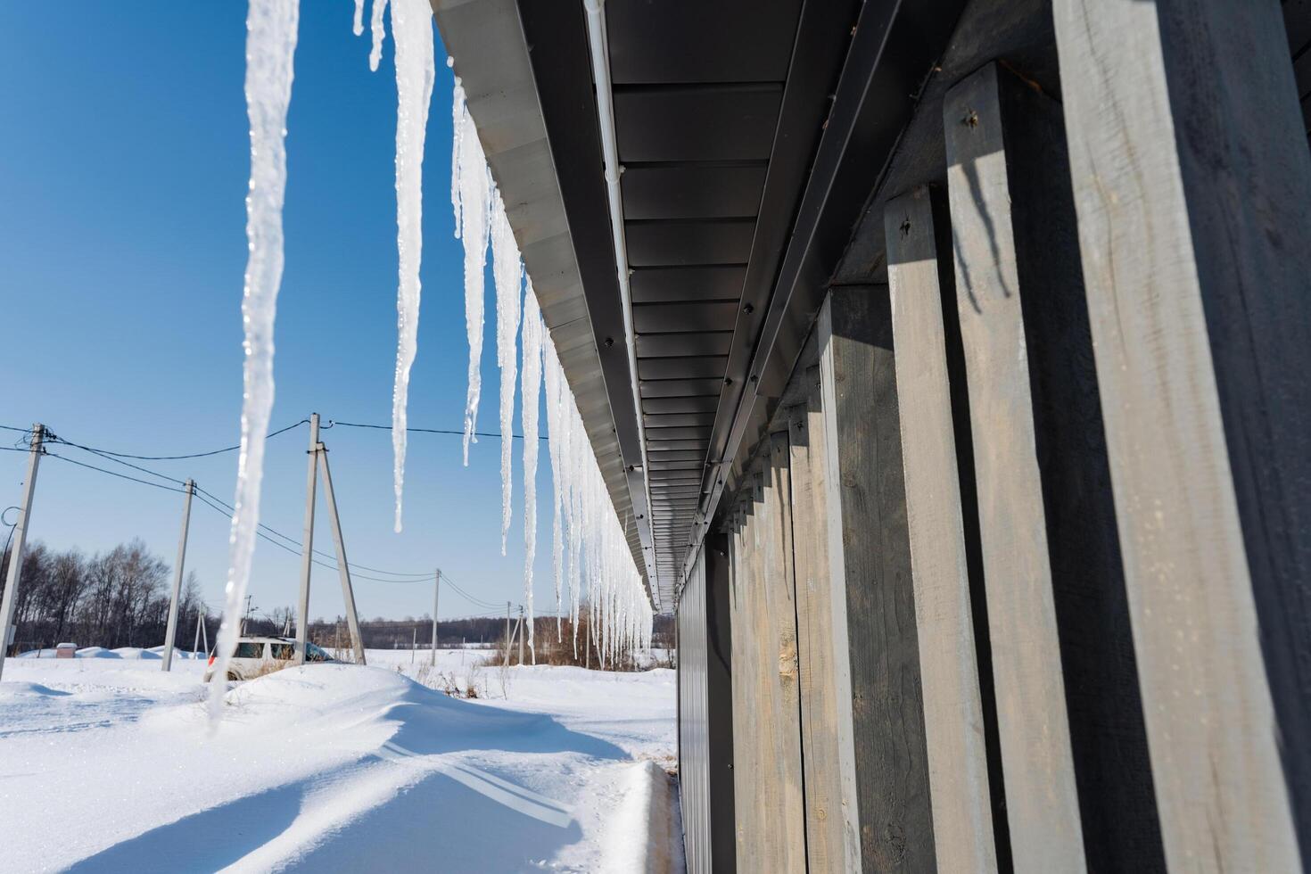 Long, sharp icicles are suspended from the edge of a building, shimmering in the bright light of the day, while snow blankets the ground all around in this wintery scene photo