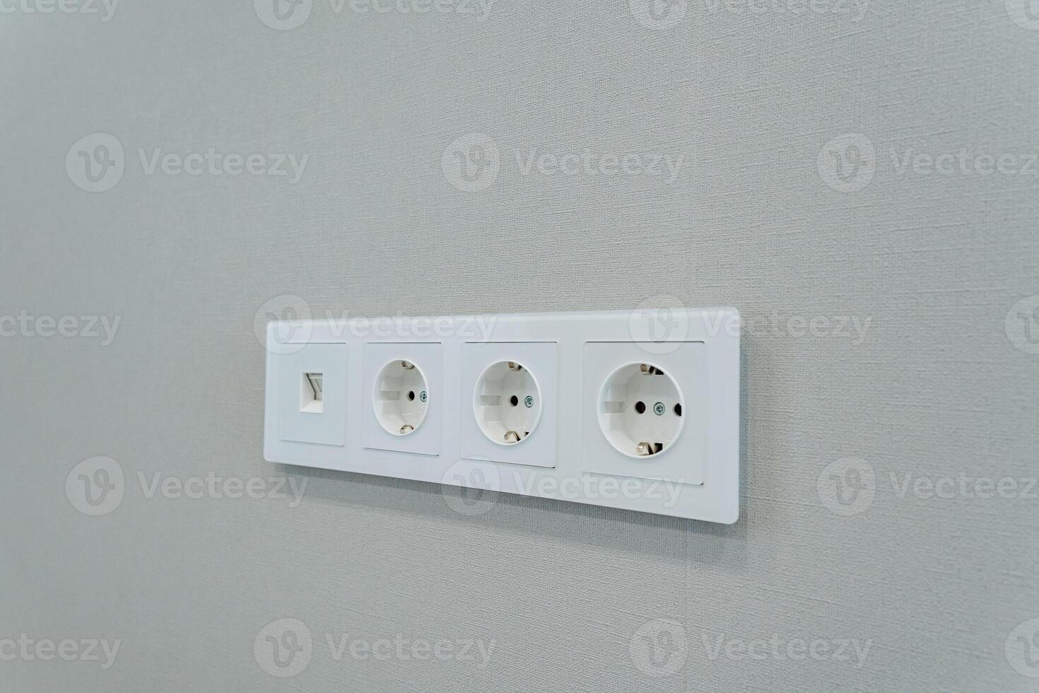 A white electrical outlet that is mounted on a gray wall is an essential component for connecting various devices to the common alternating current power supply in both homes and offices photo