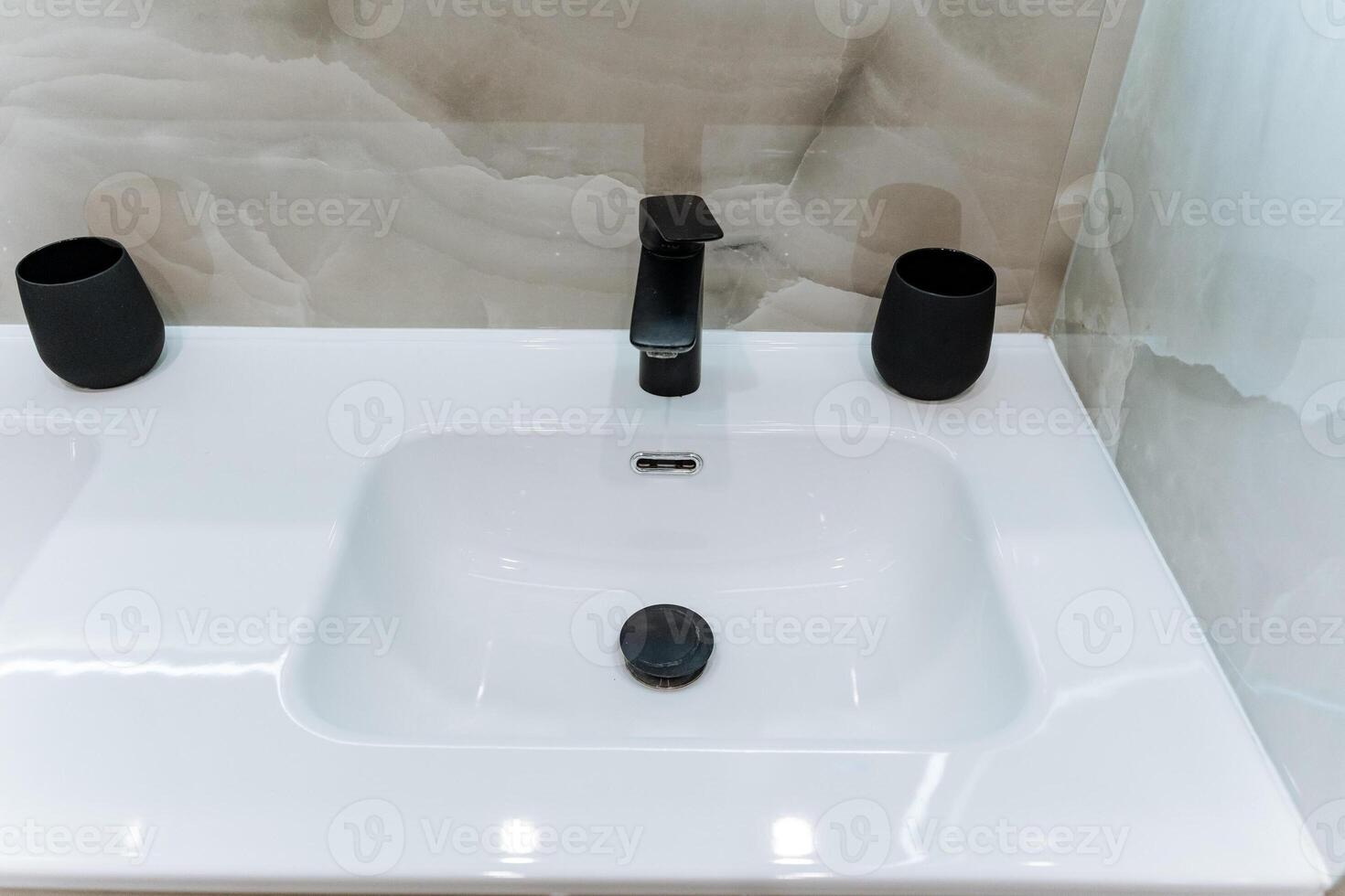 The elegant bathroom sink features a modern black faucet that complements the decor, along with two stylish black cups on the countertop, enhancing the spaces aesthetic charm photo