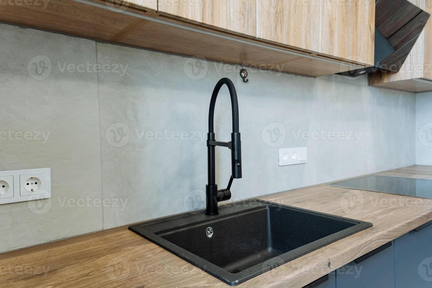 A kitchen sink equipped with a sleek black faucet is seamlessly integrated into a beautifully crafted wooden counter top that enhances the overall aesthetic of the kitchen space photo