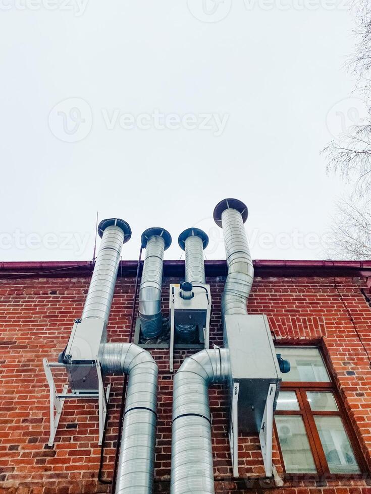 There is a brick building that has numerous pipes protruding from it, showcasing a complex network of plumbing and other utilities attached to its structure, enhancing its functionality photo