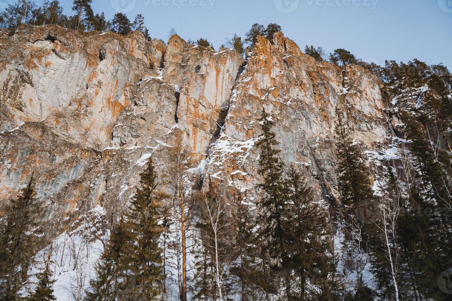 A majestic snowcapped mountain rises into the clear blue sky, surrounded by lush trees and a steep cliff, showcasing the exquisite beauty of nature in this serene setting photo