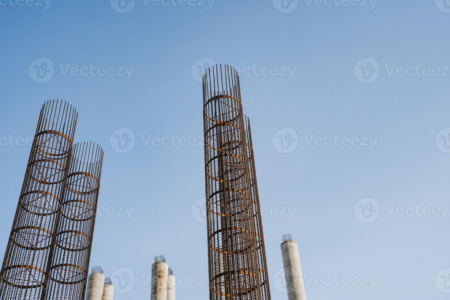 A large collection of sturdy metal pipes stands against a vibrant blue sky, showcasing an intricate display of engineering and industrial design in a highrise environment photo