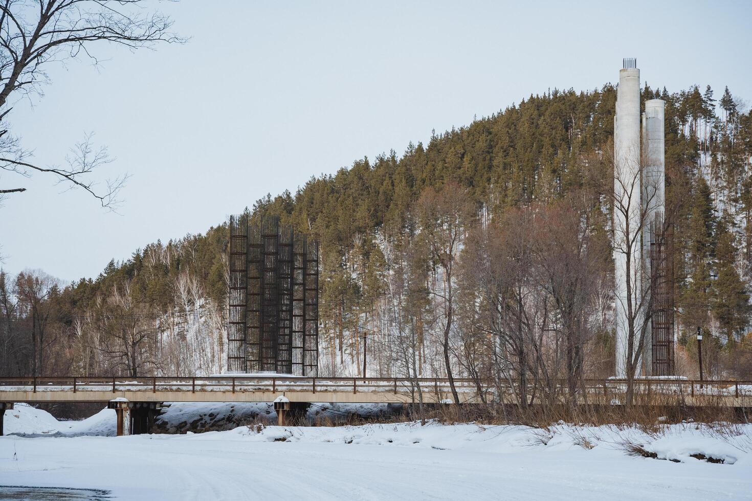 An elegant bridge spanning across a tranquil, snowy river, set against the picturesque backdrop of a majestic mountain towering in the distance, creating a stunning winter scene photo