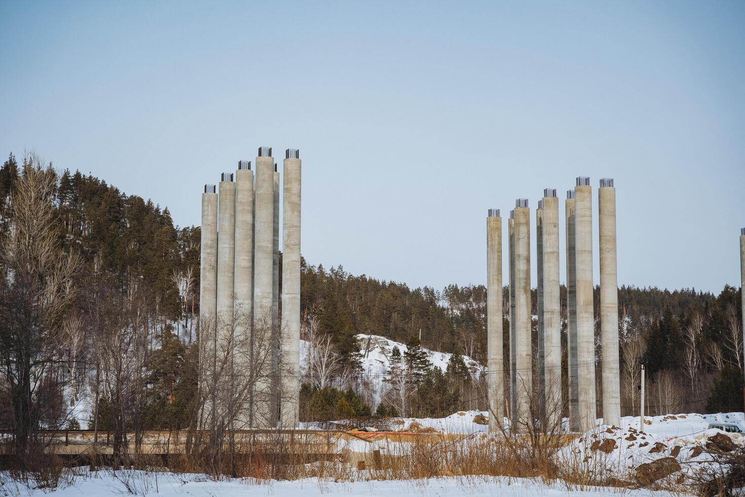 A long row of sturdy concrete pillars stands tall in the middle of a vast, snowy field blanketed in ice and snow, creating a striking contrast against the winter landscape around them photo