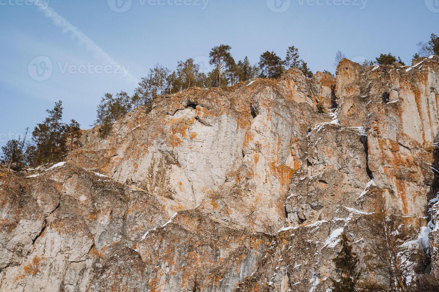A picturesque cliff adorned with vibrant trees standing tall upon it, set against a backdrop of a vast blue sky, creating a stunning natural landscape filled with beauty and tranquility photo