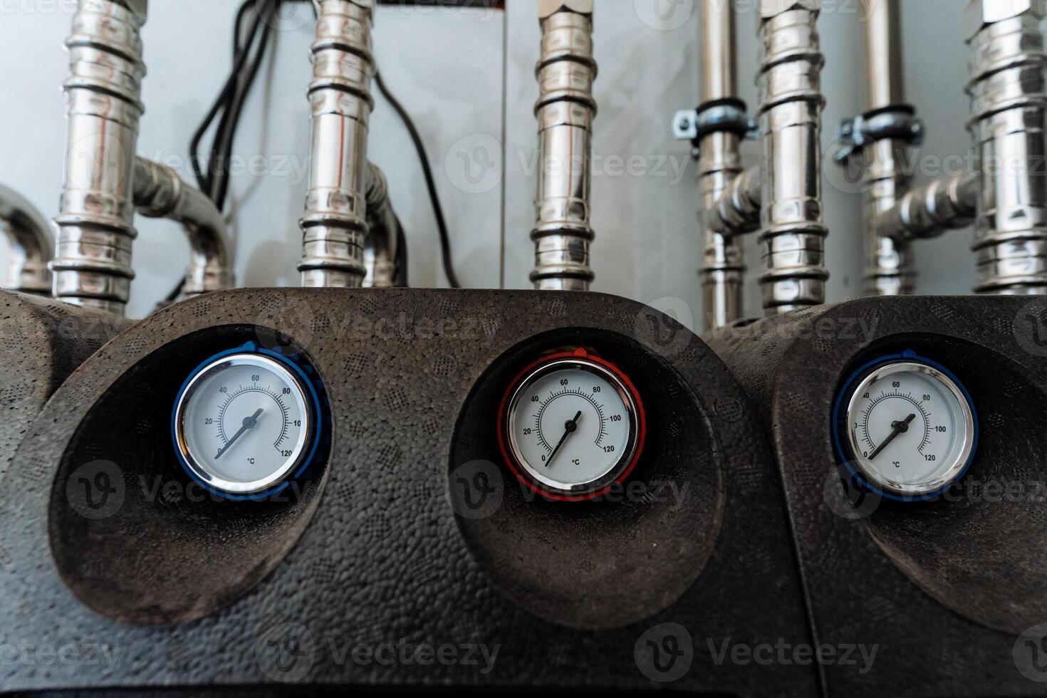 In a specific room filled with numerous pipes, there are three pressure gauges positioned closely next to each other, functioning as essential measuring instruments for the system photo
