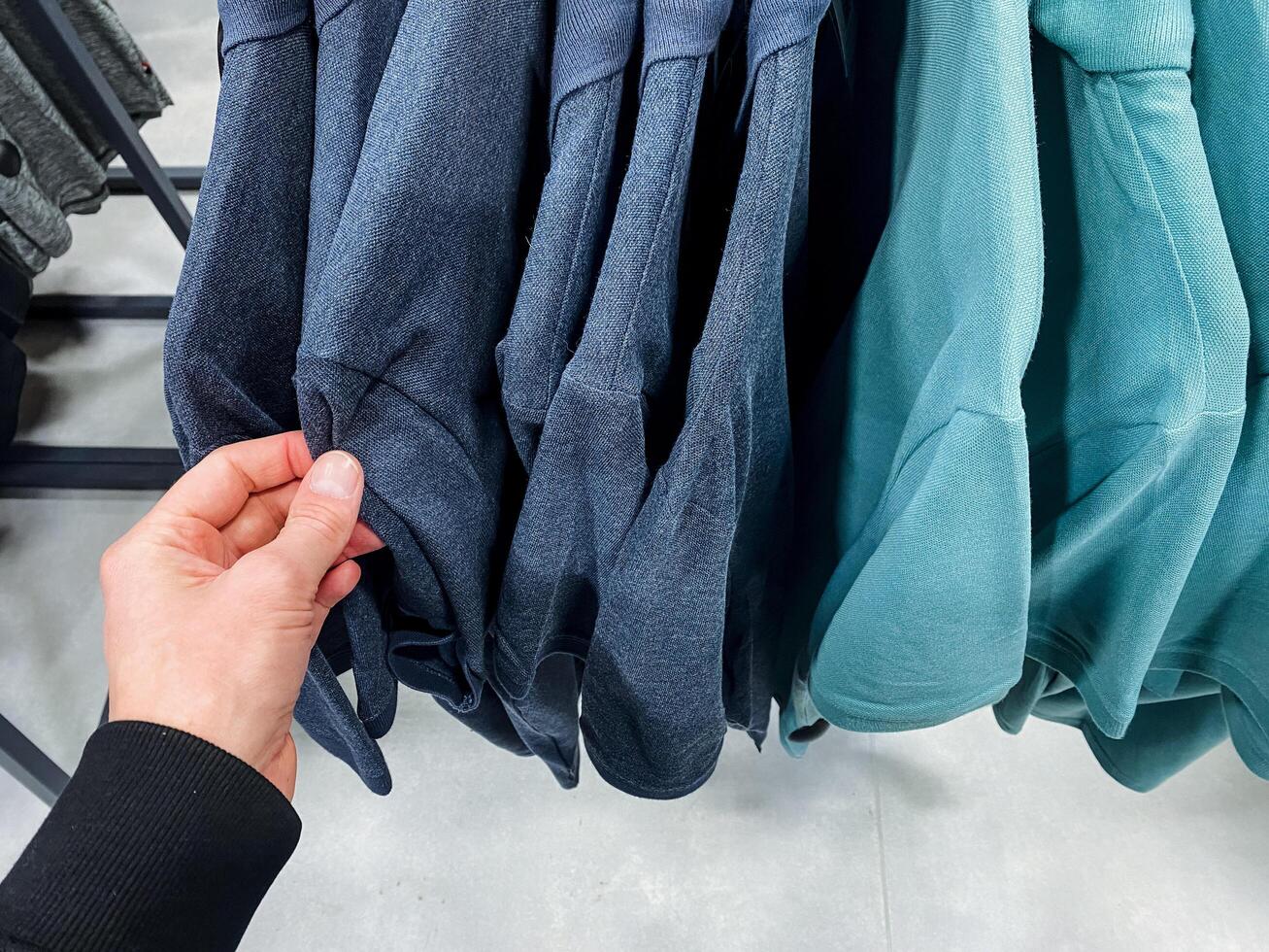 A person is currently holding a blue shirt in their hand, showcasing the vibrant color and material, which is made of denim and textile, contrasting with grey surroundings photo