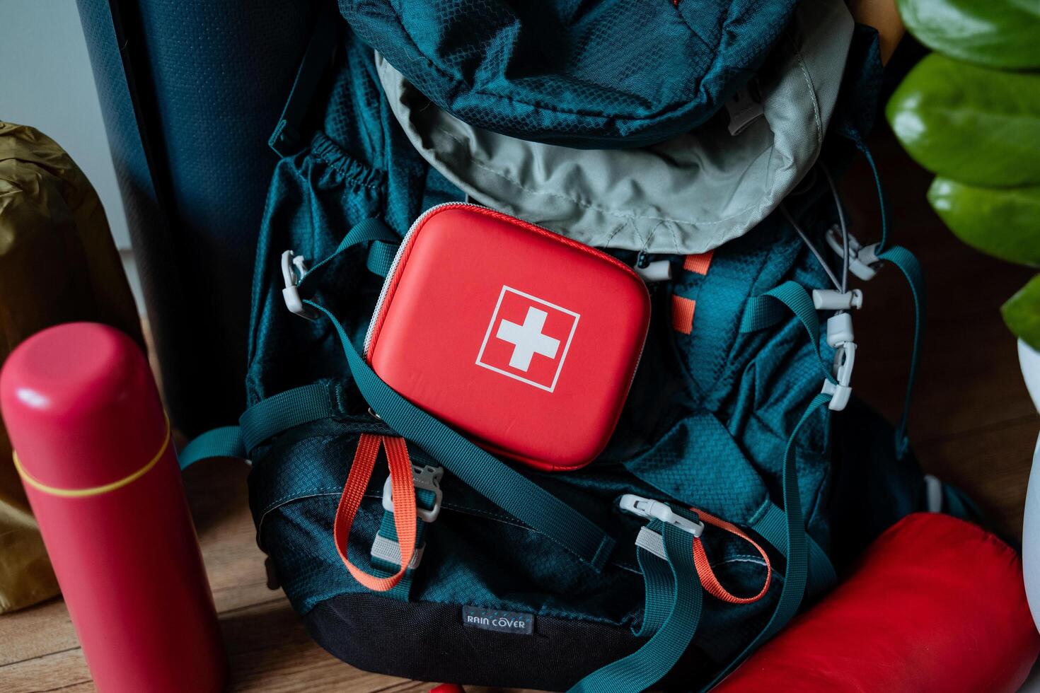 A bright red first aid kit is placed with great care on top of an outdoor backpack, which is most likely utilized for hiking or travel purposes such as excursions or journeys photo