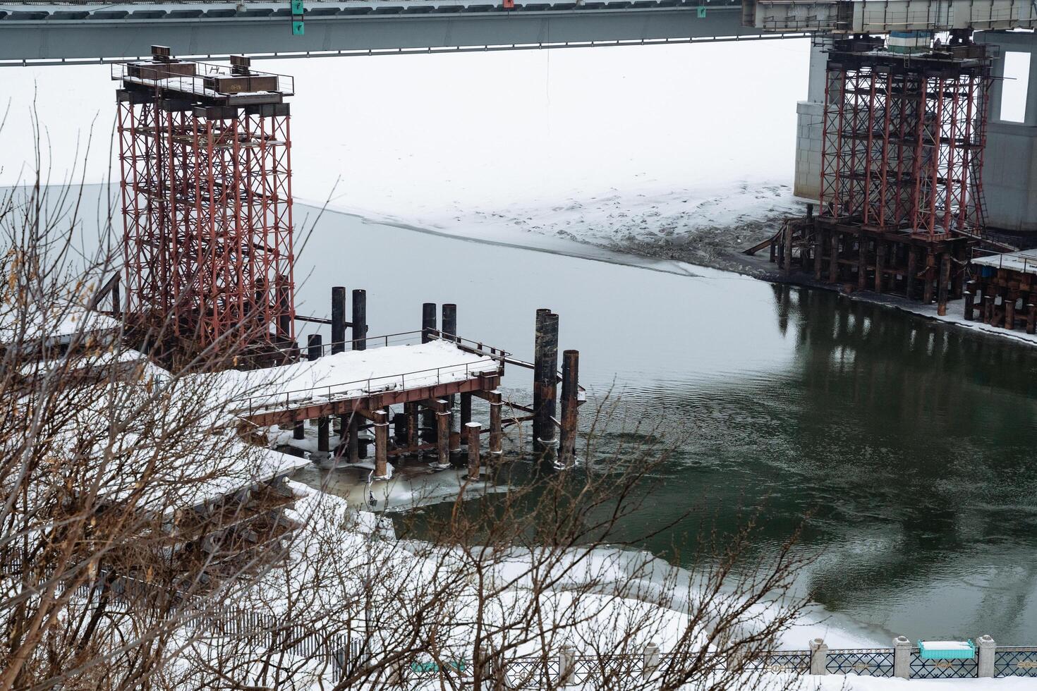 A bridge is currently under construction over a vast body of water, which could be a lake or a reservoir, showcasing impressive engineering in winter conditions with snow, mist, and fog photo