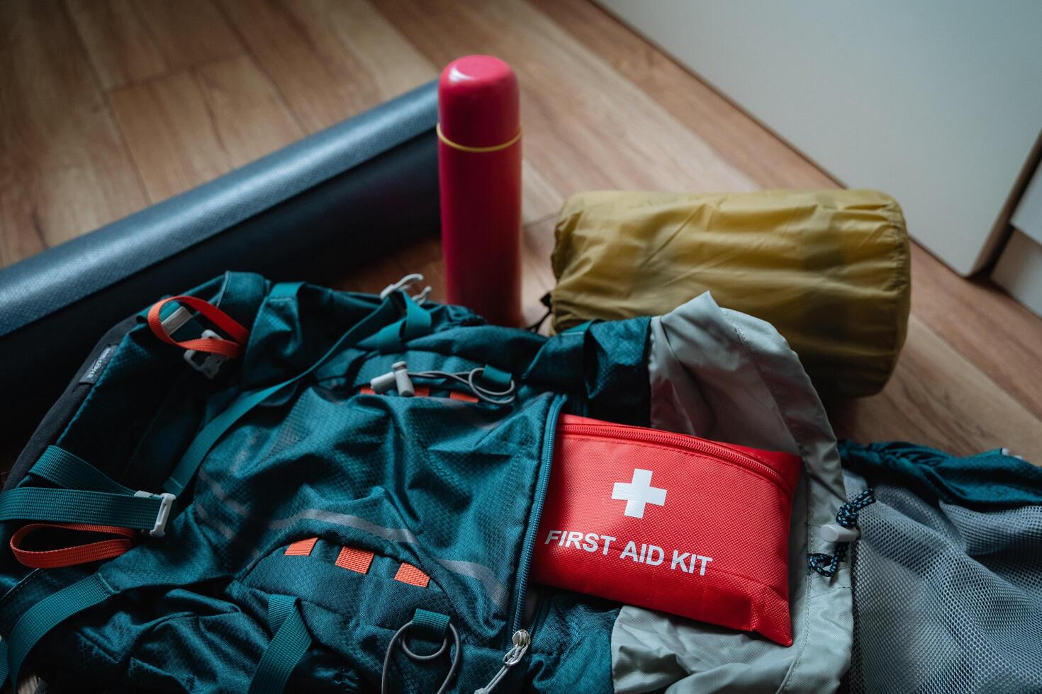 A first aid kit is conveniently placed right on top of a backpack that is likely being prepared for a trip or outdoor activity, providing easy access to essential medical supplies photo