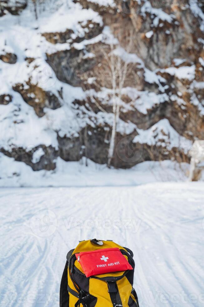 A yellow backpack with a red first aid kit, ideal for snowy outdoor adventures, especially for mountaineers exploring glacial landscapes, ensuring safety during excursions photo