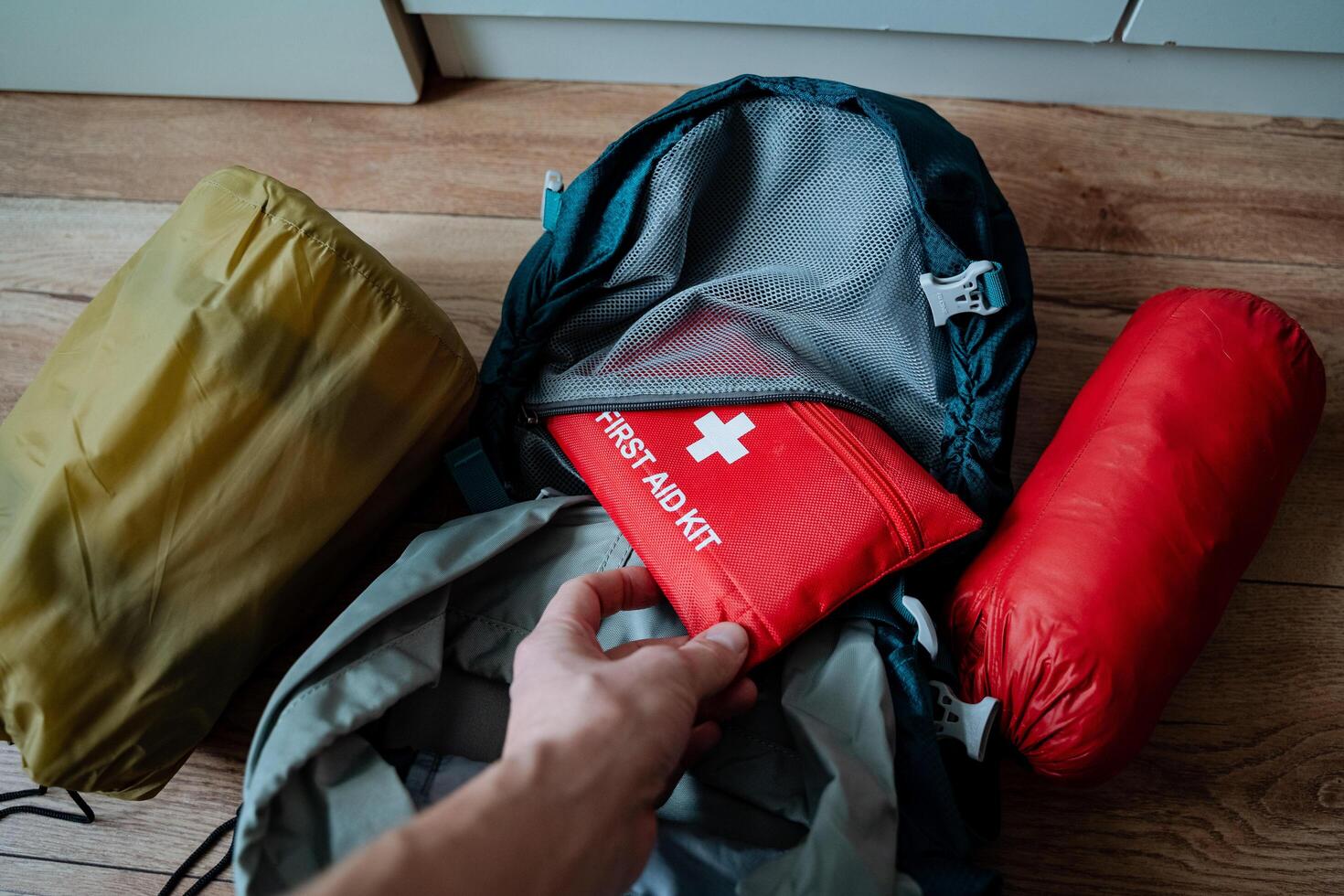 A person is carefully placing a first aid kit into a backpack as part of their preparations for a trip or an outdoor adventure, ensuring they have essential supplies on hand photo