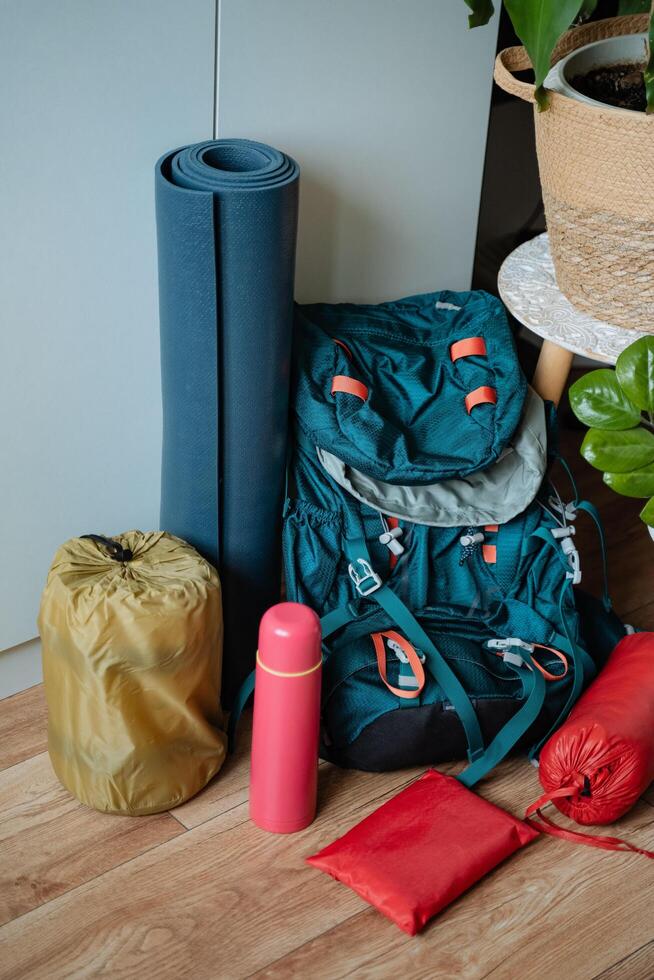 A vibrant blue backpack can be found resting on a smooth wooden floor, positioned right beside a neatly rolled yoga mat, suggesting a blend of travel and wellness activities photo
