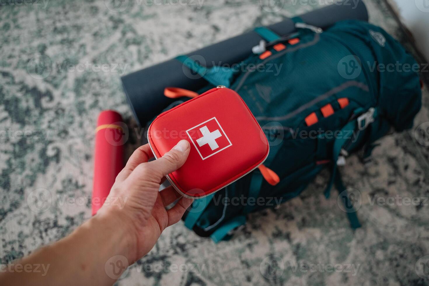 A person is holding a first aid kit in front of a backpack that seems ready for an outdoor adventure, emphasizing the importance of safety while engaging in various activities outdoors photo