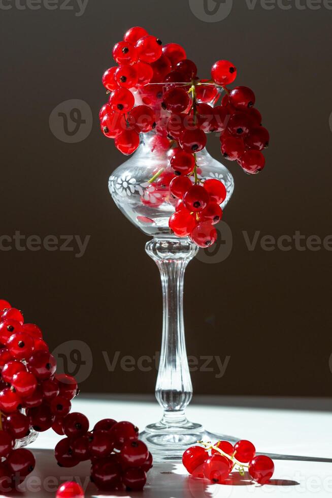 View of a crystal glass filled with ripe red currants on a dark background photo
