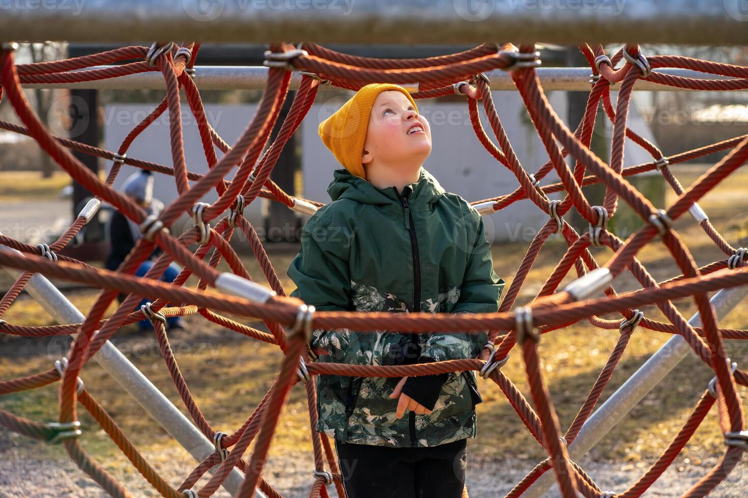 A child wearing a yellow cap climbs an alpine trellis on a playground photo