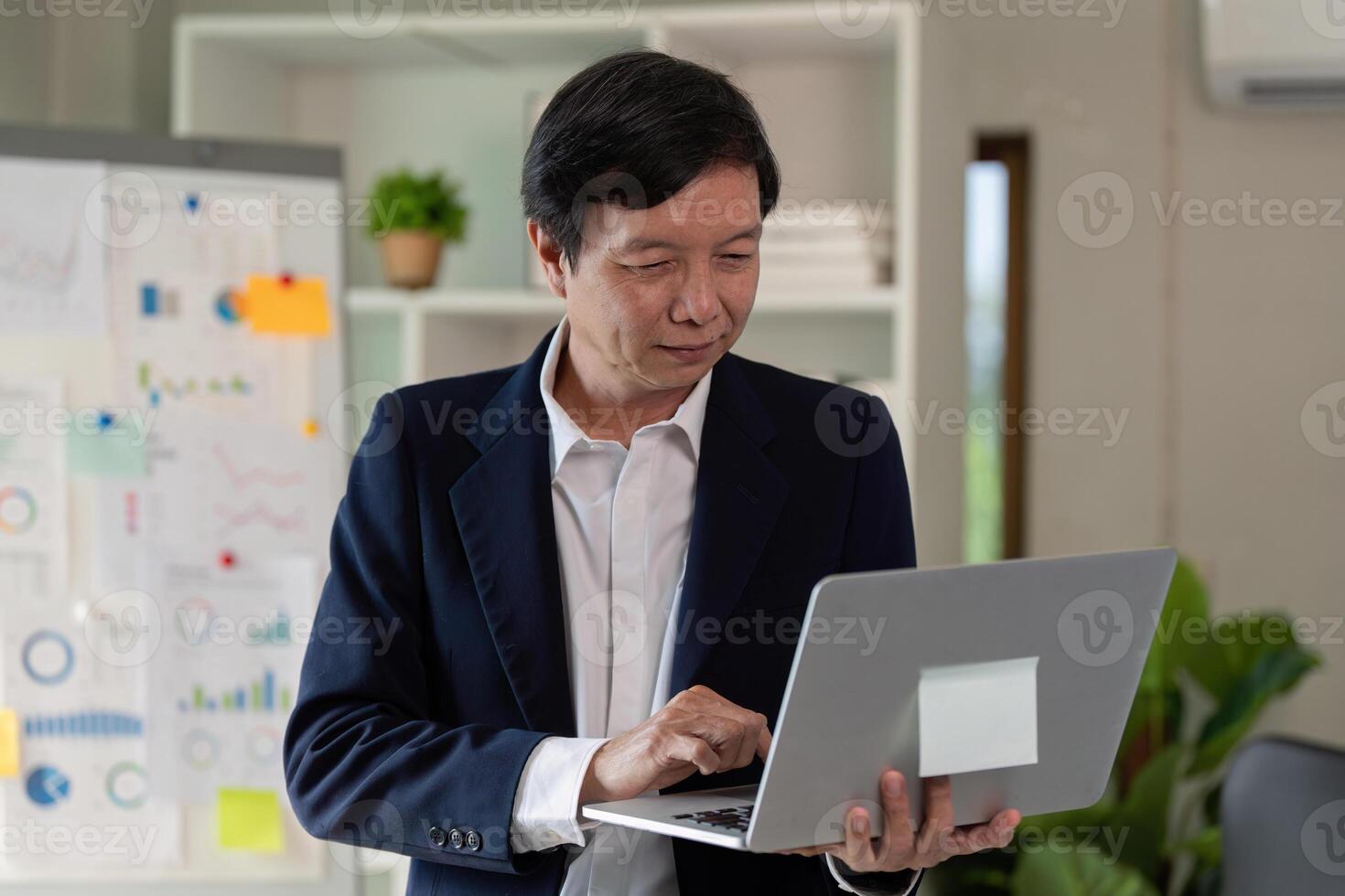 Elderly professional using a laptop while standing in a modern office. photo