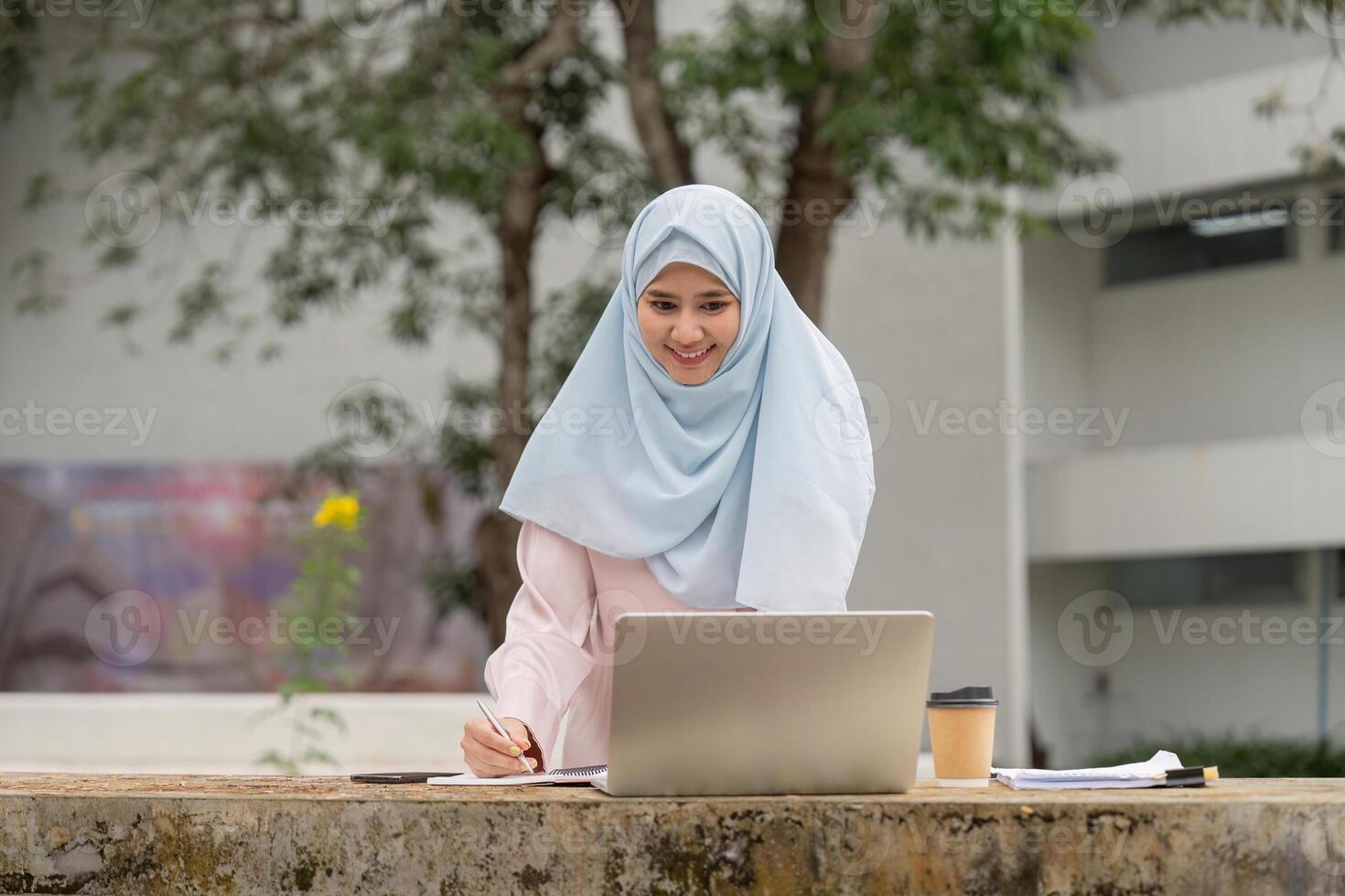 Smiling Muslim woman studying with a laptop outdoors, representing determination and growth in her academic journey. photo