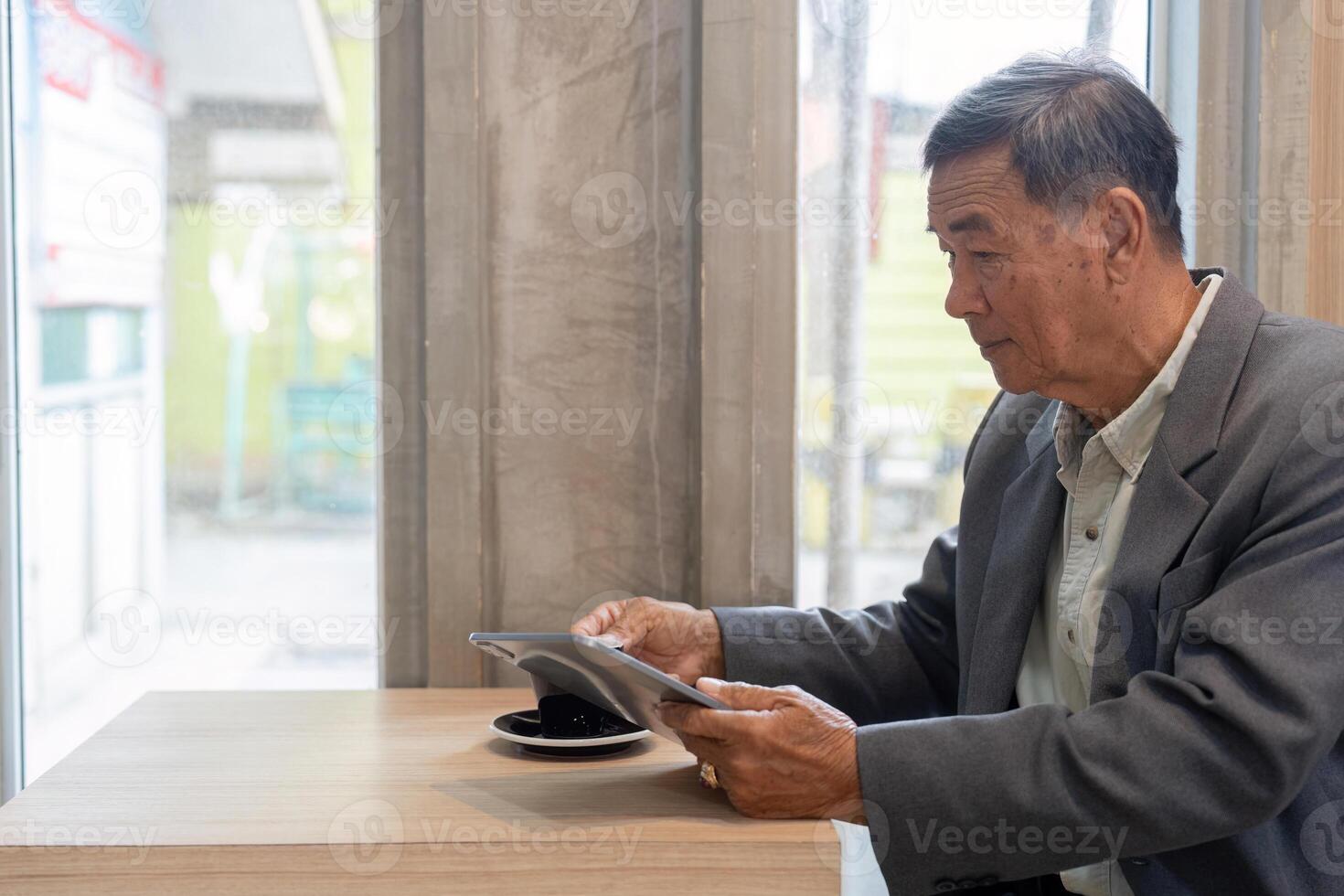 Senior businessman focused on a tablet while enjoying coffee in a modern cafe setting. photo