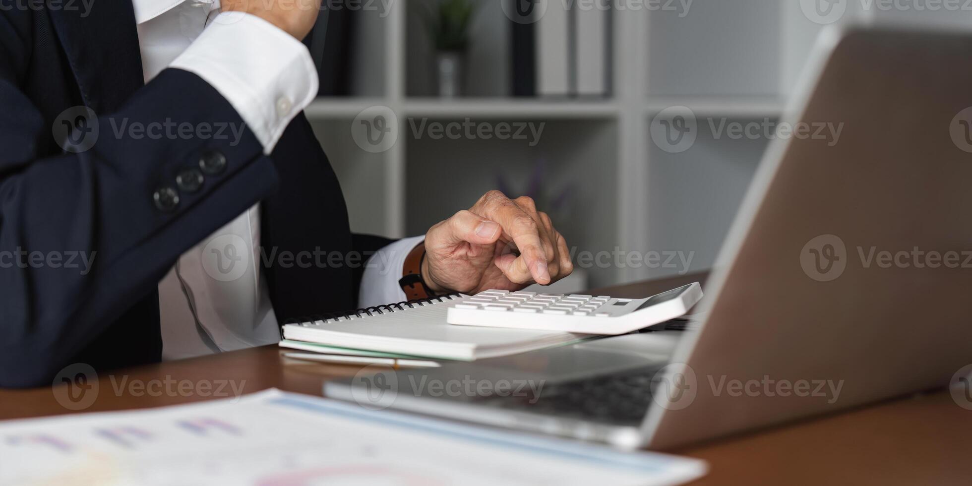 Close-up of elderly businessman using a calculator and notes in a modern office setting. photo