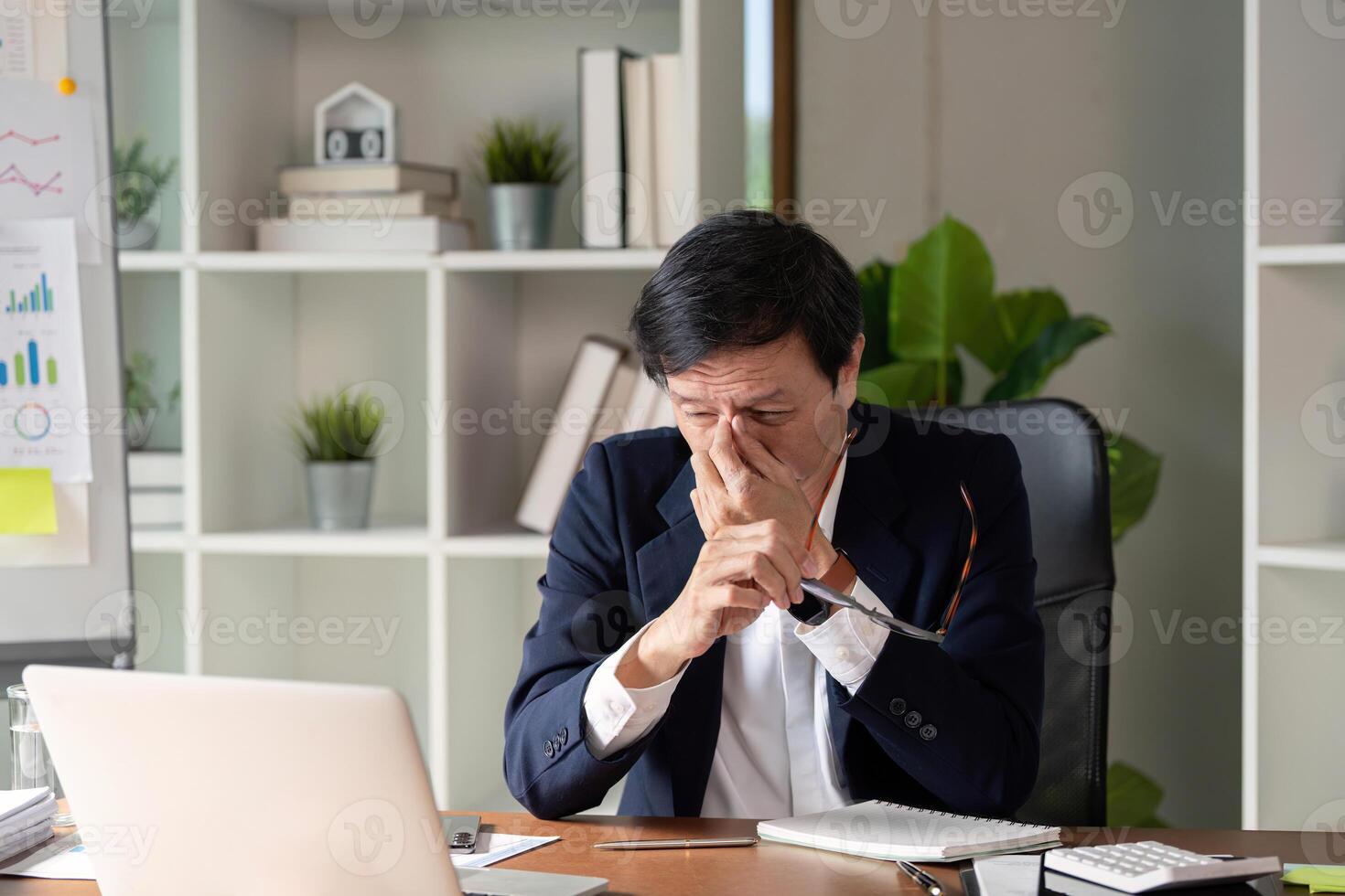 Elderly professional showing signs of stress while analyzing data in a business environment. photo