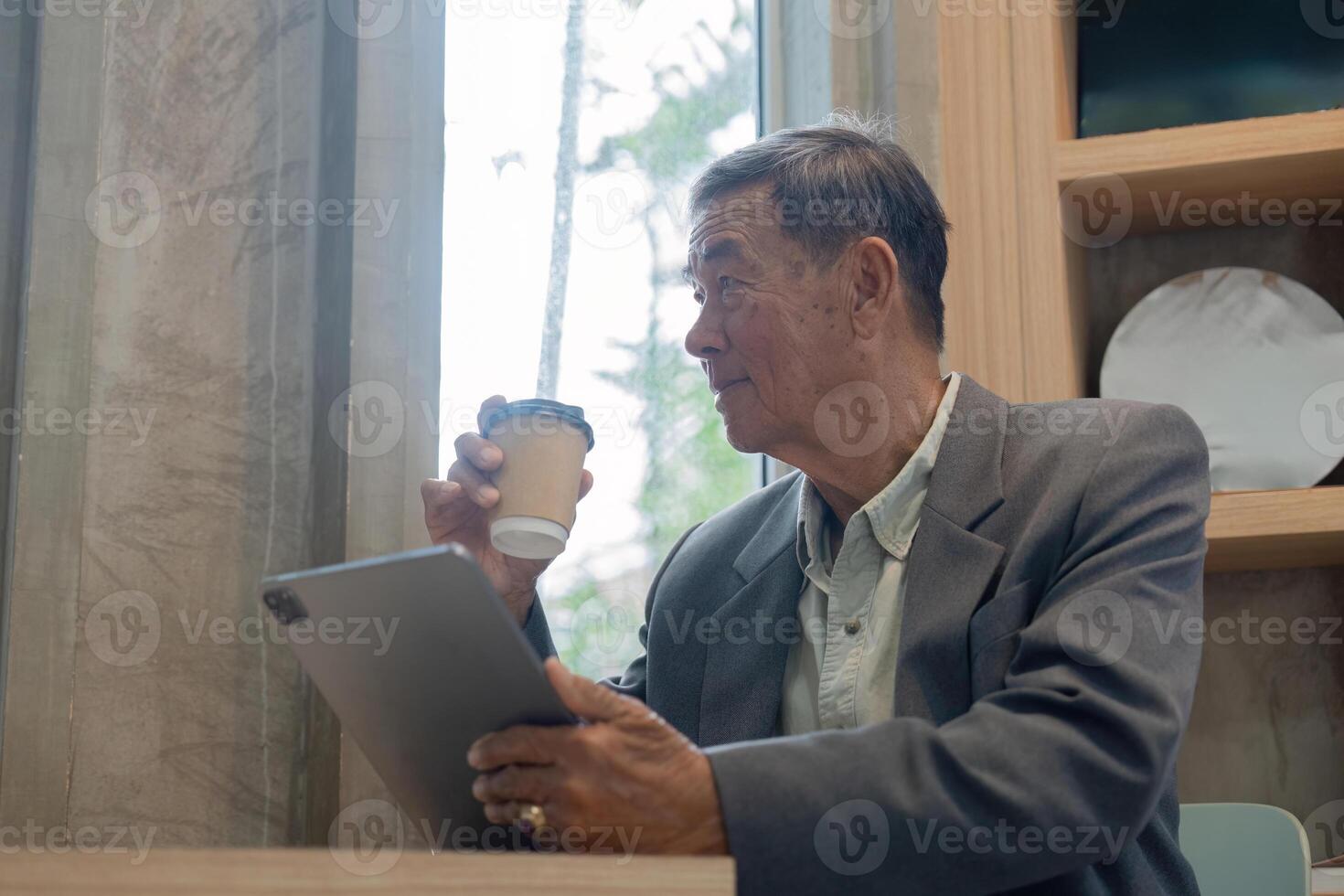 Elderly man enjoying coffee while using a tablet, gazing out the window in a cafe. photo