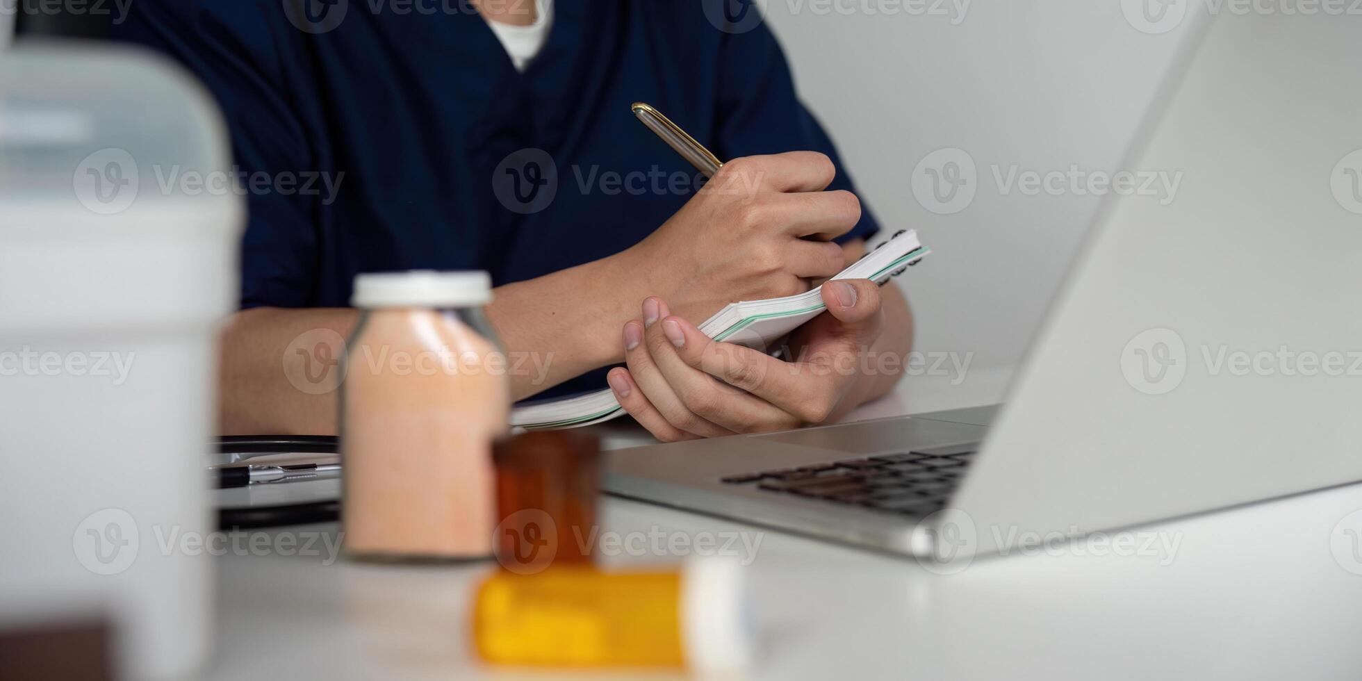 Medical student taking notes while studying medications at a desk with a laptop. photo