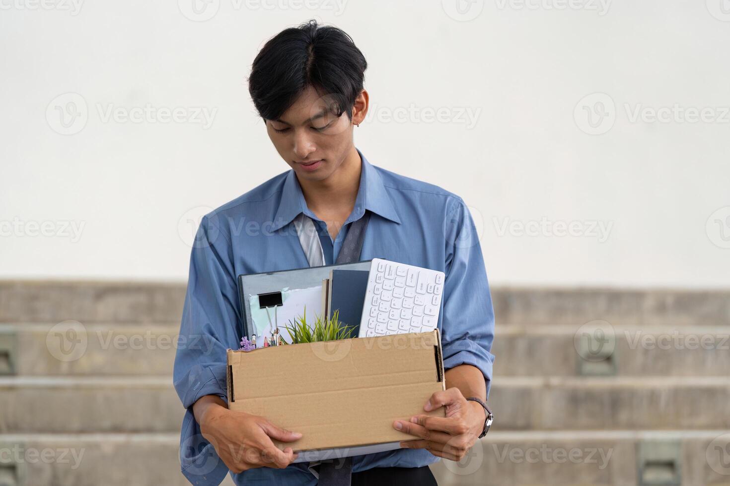 Young man leaving office with personal belongings in a box after resignation, reflecting on career transition. photo