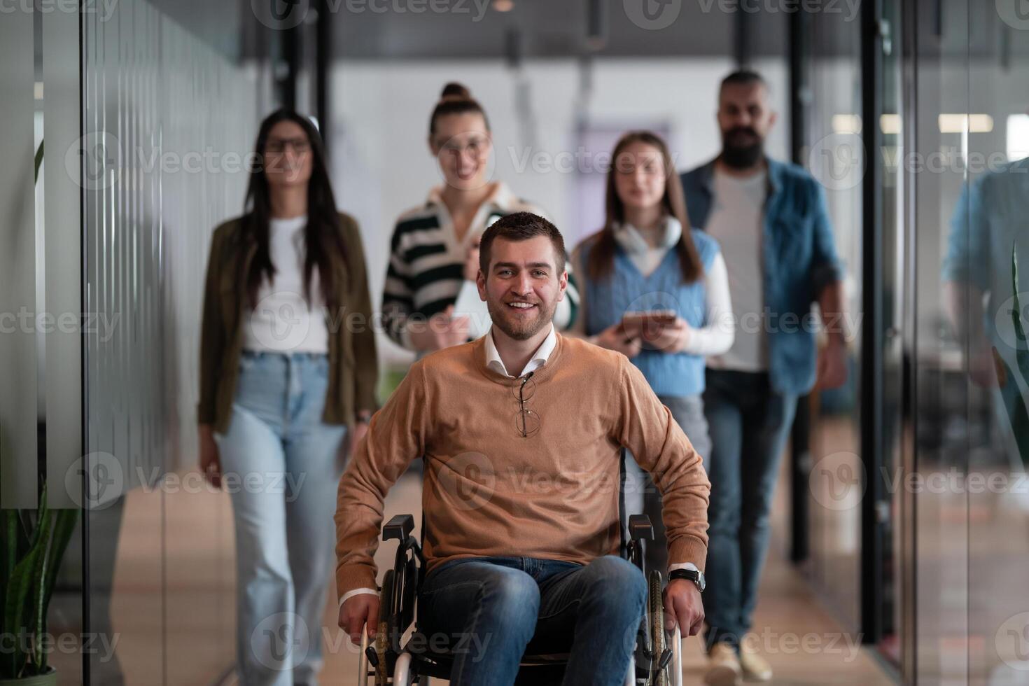 A businessman with disability in a wheelchair is surrounded by supportive colleagues in a modern office, showcasing the strength of teamwork, inclusivity, and empowerment in the face of challenges. photo