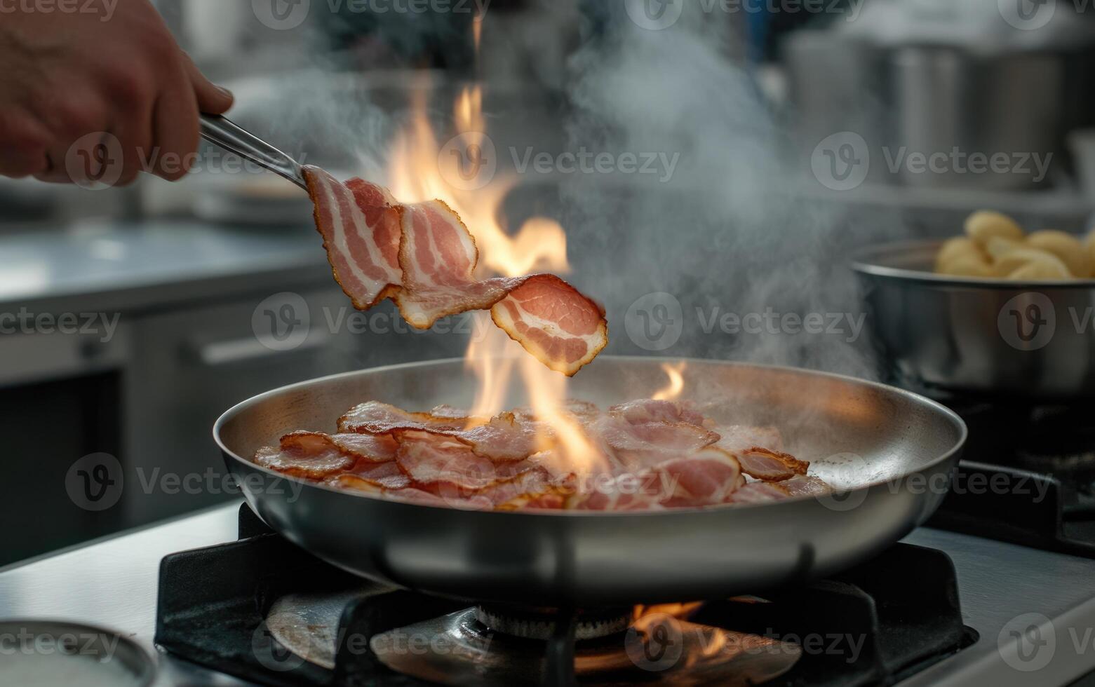 A chef skillfully flips slices of bacon in a frying pan over high heat, creating flames and smoke in a busy kitchen setting. The atmosphere is vibrant and filled with cooking activity photo