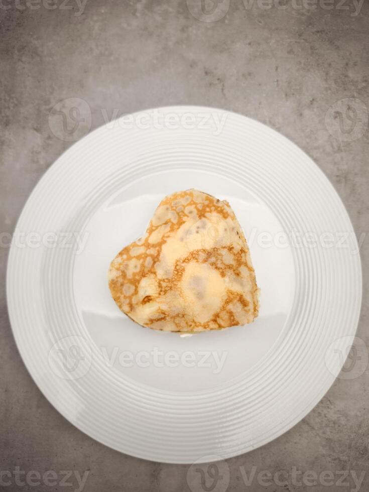 Delicate heart shaped crepes with yogurt folding elegantly over white plate, resting on textured gray surface for Mother's Day Valentines copy space photo