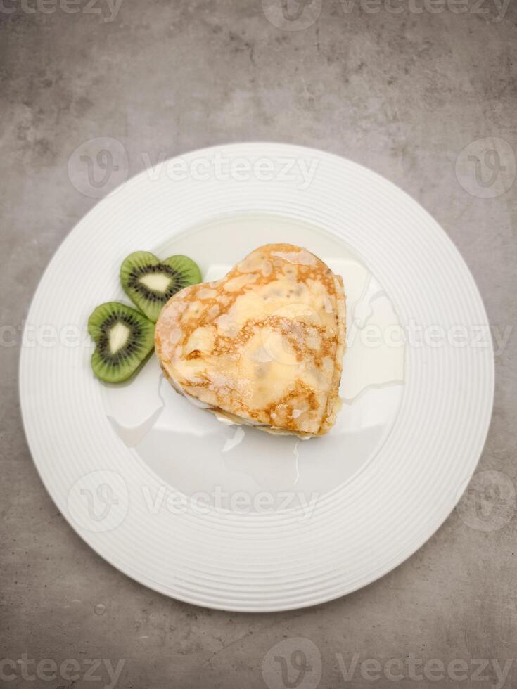 Heart shaped crepes with white yogurt, pancakes drizzling honey, garnished with kiwi slices, presenting romantic breakfast on pristine white ceramic plate for Mother's Day Valentines copy space photo