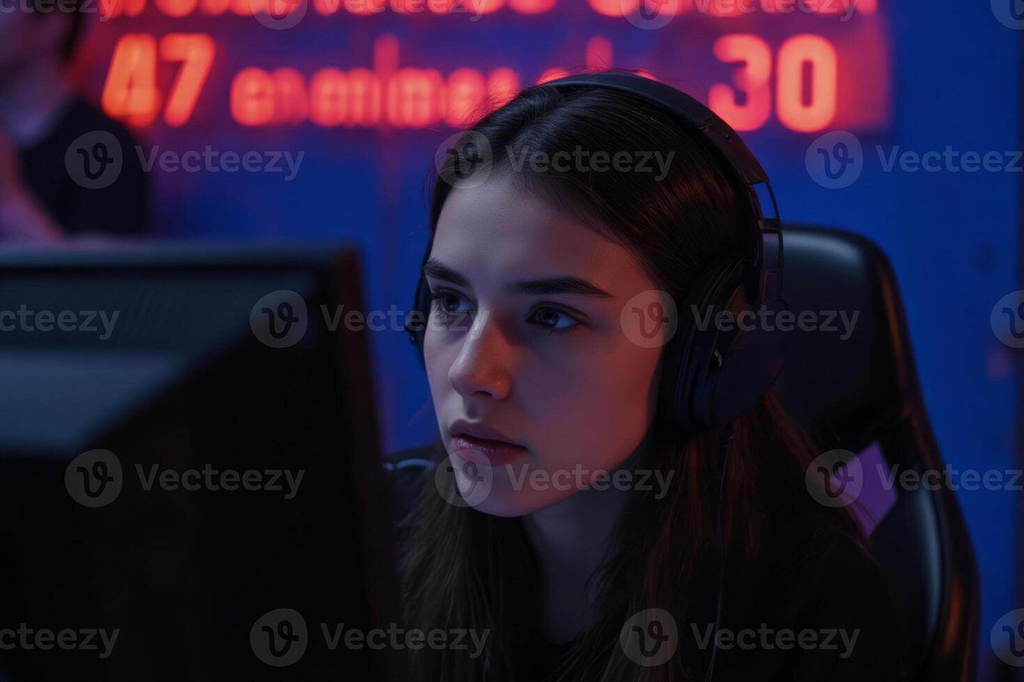 A white girl, 19 years old with long brown hair, wearing a headset in front of a computer screen, in a gaming room photo