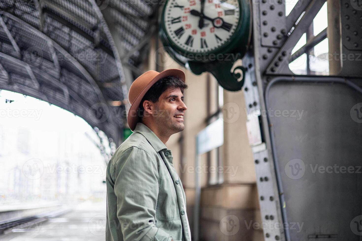 latin Tourist wearing hat waiting for train looking at station clock photo