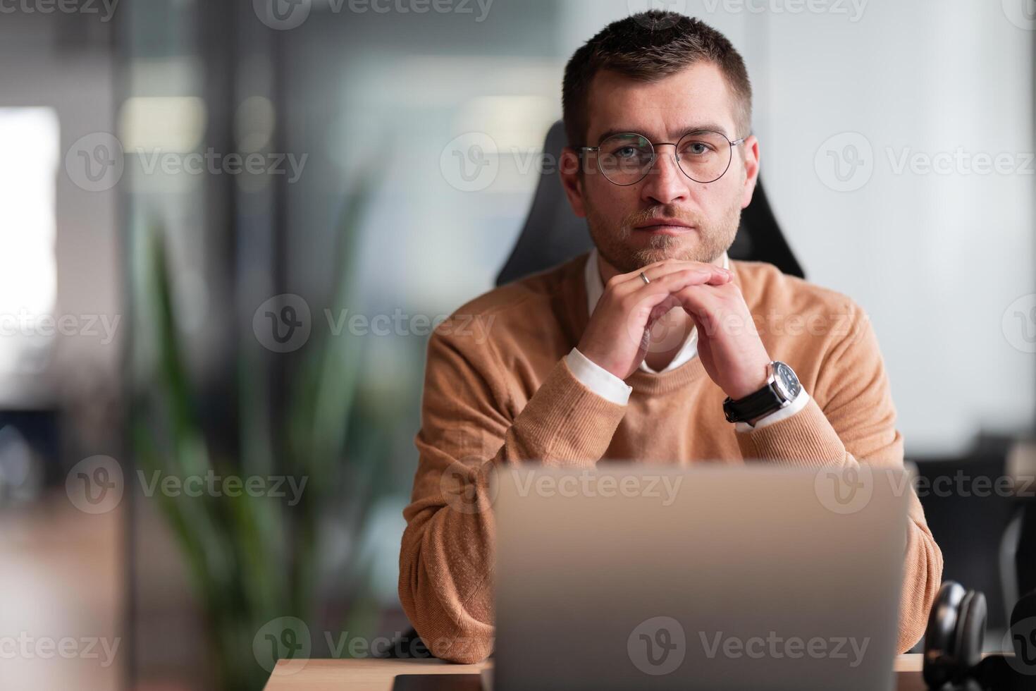Smart looking focused businessman working on a laptop and thinking. Millennial managing family budget, handling financial paperwork, and tracking expenditures on a laptop at a modern open space office photo